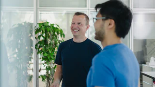 Mitarbeiter in der Softwareentwicklung lächeln und schauen dabei auf ein Whiteboard
