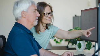 Mitarbeiter in der Softwareentwicklung arbeiten zusammen am Computer; eine zeigt auf den Bildschirm