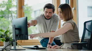 Mitarbeiter der Qualitätssicherung zeigen zusammen auf den Computer